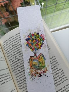 an open book with a watercolor painting on it's cover and a hot air balloon in the shape of a house