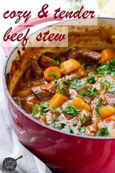 a red pot filled with beef stew on top of a white table next to a fork