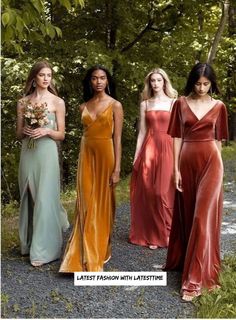 four women in long dresses standing on a dirt road with trees and bushes behind them