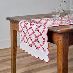 a red and white table runner on top of a wooden table next to two glasses