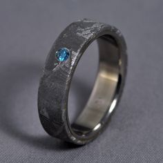 a wedding ring with a blue diamond in the center on a gray clothed surface