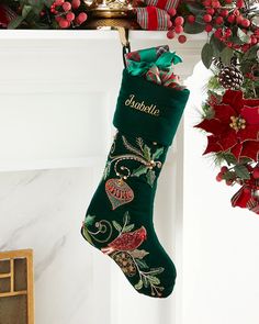 a christmas stocking hanging from a mantel decorated with holly and poinsettis