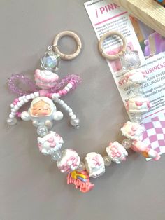 a pink and white beaded keychain with a baby doll hanging from it's side