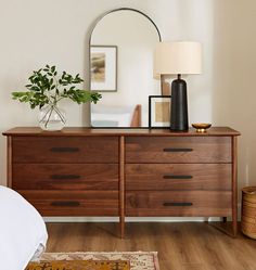 a dresser with a mirror, lamp and vase on it in a living room area