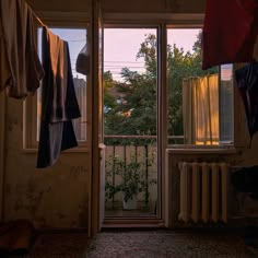 an open door leading to a balcony with clothes hanging on the line and trees in the background