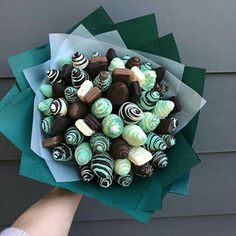 a person holding a bouquet of chocolates and candies in green paper wrappers