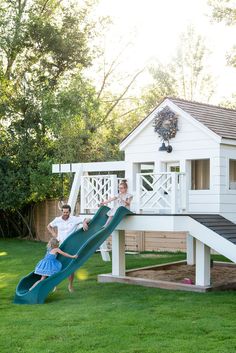 a man and his daughter playing on a slide in the yard with a house behind them