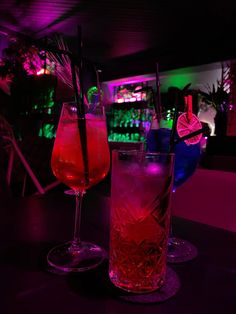 two glasses filled with drinks sitting on top of a table in front of a bar