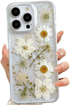 a woman's hand holding an iphone case with white flowers on the front and gold glitter