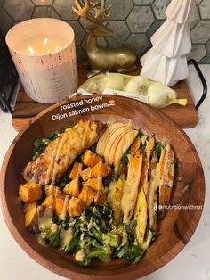 a wooden bowl filled with lots of food next to a candle on a counter top