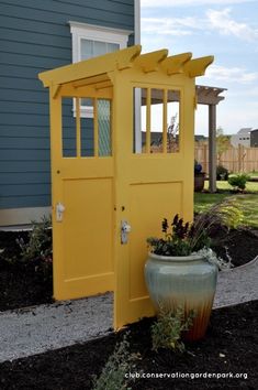 a yellow outhouse sitting next to a flower pot