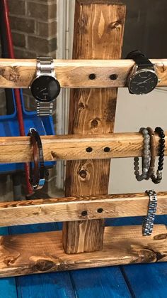 a wooden rack with watches and bracelets hanging from it's sides on a blue table