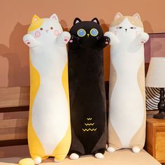 three stuffed cats sitting next to each other on a bed in front of a lamp