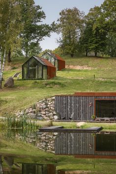 two small houses sitting next to each other on top of a lush green hillside near water