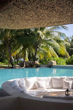 an outdoor lounge area next to a swimming pool with palm trees in the back ground