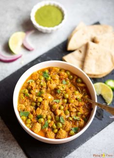 a white bowl filled with curry next to pita chips and limes on the side