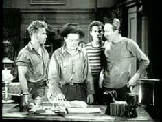 four men are standing around a table in a kitchen, one is looking at the camera