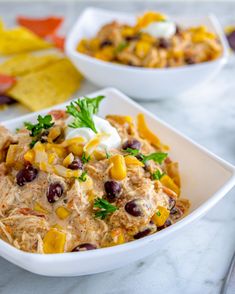 two white bowls filled with food sitting on top of a marble counter next to chips