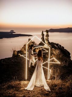 a bride and groom standing on top of a hill with their lights in the shape of houses