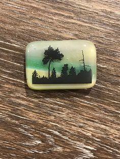 a green and black glass cabochle with trees in the background on a wooden surface