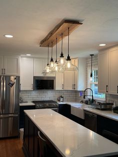 a kitchen with white cabinets and marble counter tops, lights hanging from the ceiling over the island