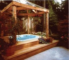 a wooden gazebo with a hot tub in the middle surrounded by flowers and trees