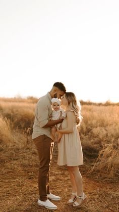 a man holding a baby in his arms while standing next to a woman on the ground