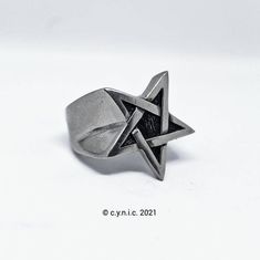 a silver ring with an inverted star on the front and center, sitting on a white surface