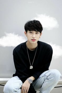 a young man sitting on top of a toilet wearing a black shirt and blue jeans