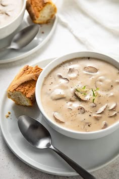 a bowl of soup on a plate with two spoons next to it and bread