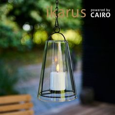 a lit candle is hanging from a glass lantern on a patio table with the words klarus written above it