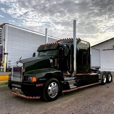 a black semi truck parked in front of a building with a cloudy sky behind it