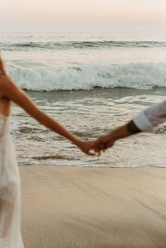 a couple holding hands while walking on the beach