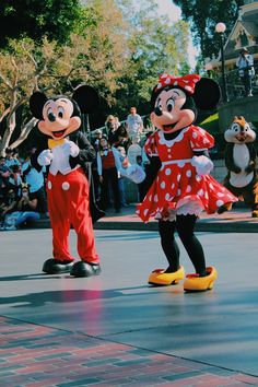 two mickey and minnie mouse characters standing in front of a crowd