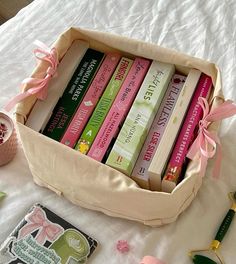 a box filled with lots of books on top of a white bed covered in pink ribbon