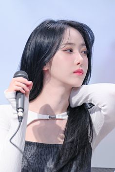 a woman with long black hair holding a microphone in front of her face and looking off to the side