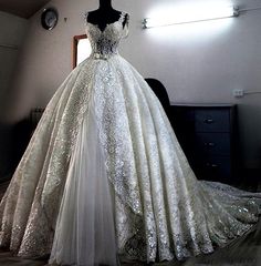 a white wedding dress on display in a room with a black dresser and mirror behind it