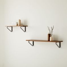 two wooden shelves with black metal brackets and vases on them against a white wall