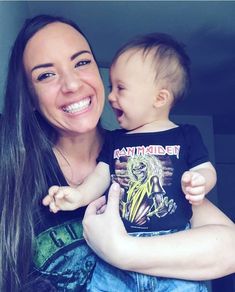 a woman holding a baby in her arms and smiling at the camera while she holds it up