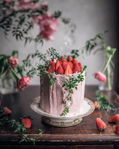 a pink cake with fresh strawberries on top and greenery around the edges, sitting on a wooden table