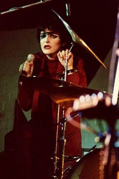 a woman playing the drums in front of a microphone and drum sticks on her head