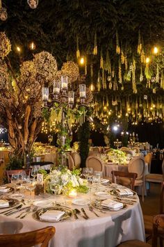 a dining room with tables and chairs covered in white linens, lit by hanging lights