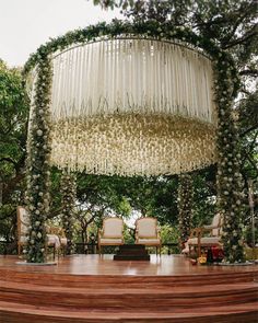 an outdoor ceremony setup with chairs and flowers on the ceiling, surrounded by greenery