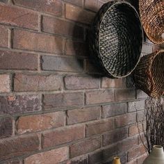 three baskets are hanging on the brick wall next to two vases and a basket