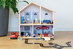 a toy house with cars and people in it on the floor next to a potted plant