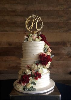 a white wedding cake with red flowers and a monogrammed s on the top