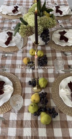 the table is set with plates, silverware, fruit and a candle on it