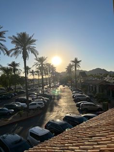 the sun is setting over a parking lot with cars parked on it and palm trees in the background