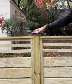 a person holding onto a wooden fence with their hand on the top part of it