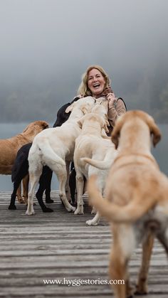 a woman is hugging her dogs on the dock while they are all huddled up together